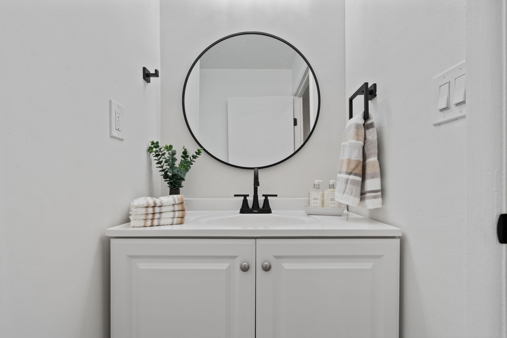 Vanity with a white countertop and integrated sink, framed by a circular black-rimmed mirror