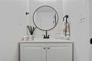 Vanity with a white countertop and integrated sink, framed by a circular black-rimmed mirror