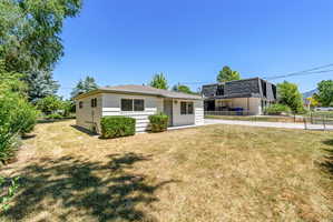 White siding exterior with multiple windows, a grey shingle roof, and established foundation plantings