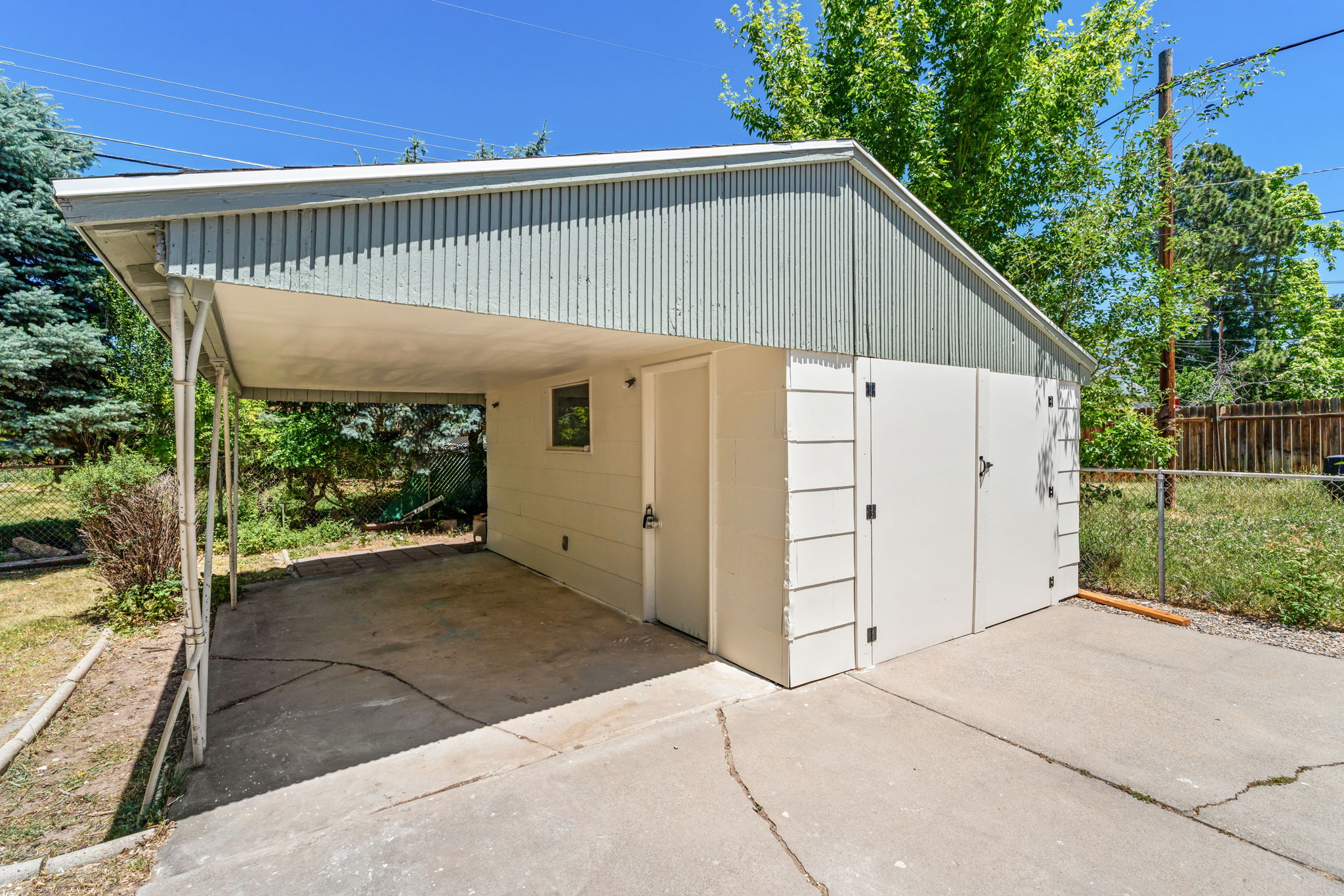 Dedicated carport structure featuring a concrete pad, painted white siding, a contrasting light green corrugated metal gable, and dual exterior storage access points