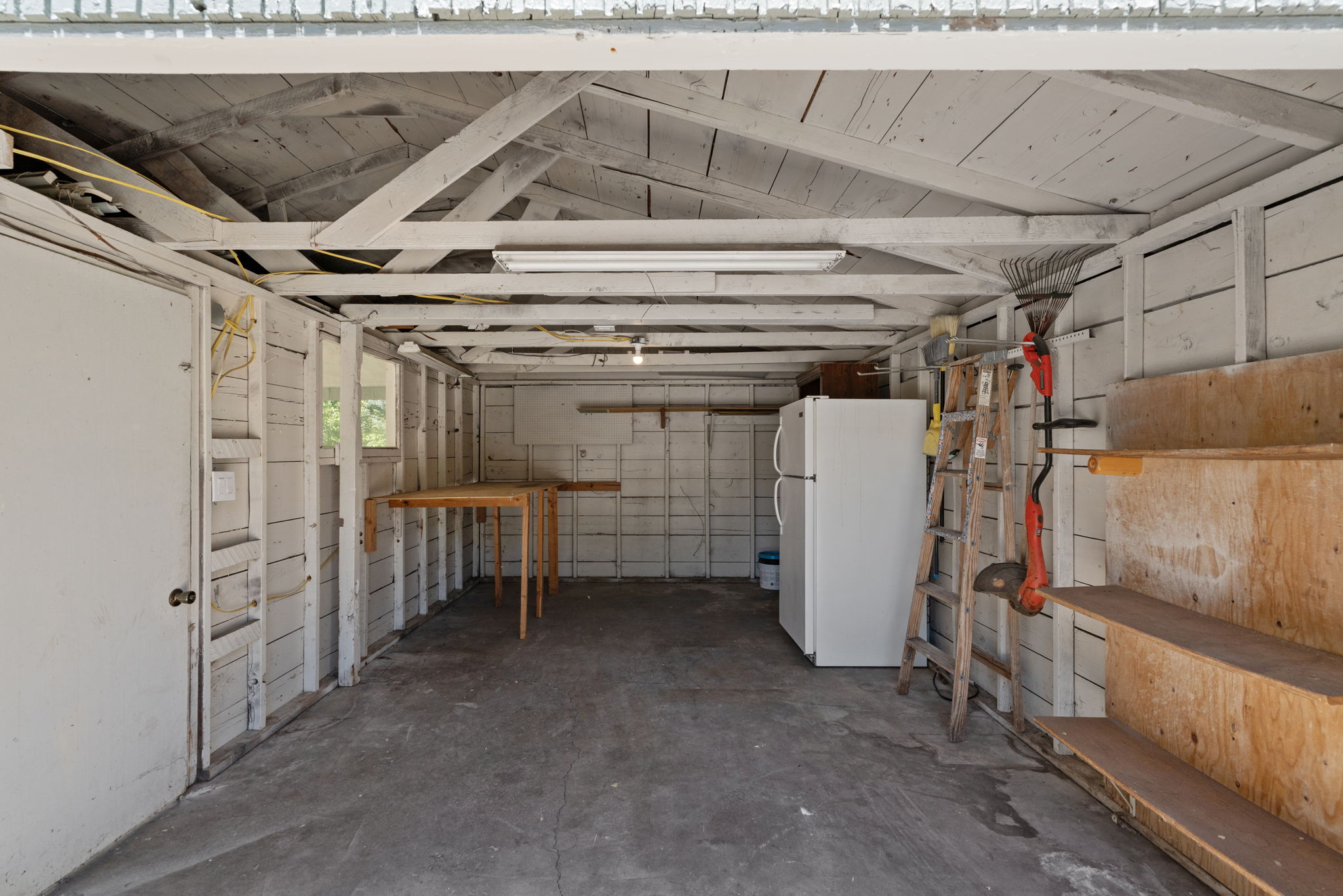 Spacious garage with concrete flooring, exposed ceiling rafters, and white painted wooden walls