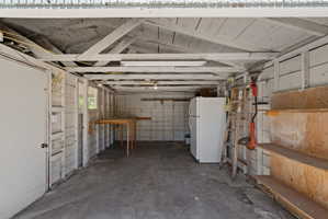 Spacious garage with concrete flooring, exposed ceiling rafters, and white painted wooden walls