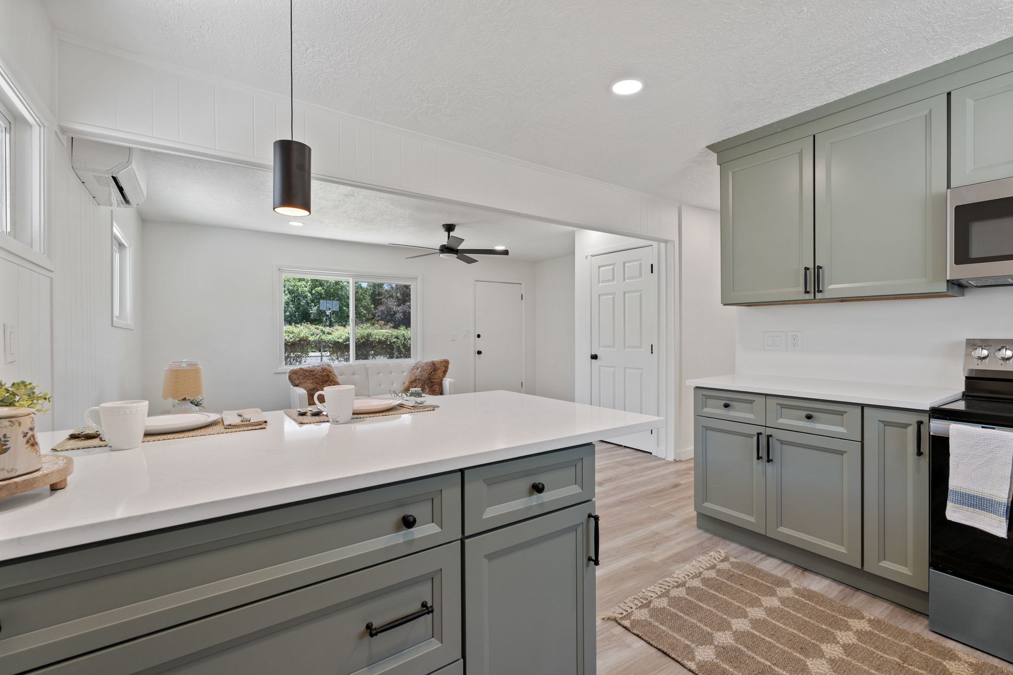 Kitchen featuring a spacious island with a white countertop, contemporary pendant lighting, light green cabinetry, stainless steel appliances, and wood-finish flooring