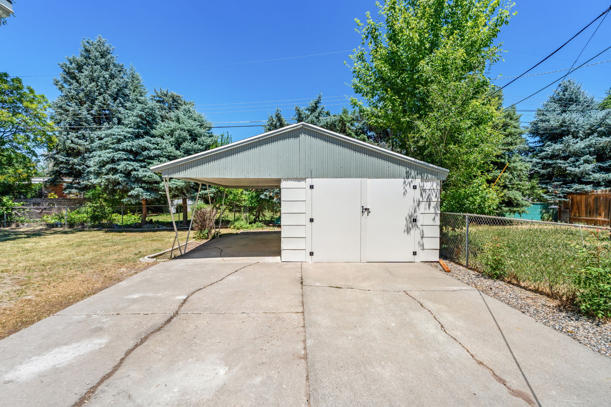 Gable-roof carport with an attached storage shed, featuring white double doors and shingle siding