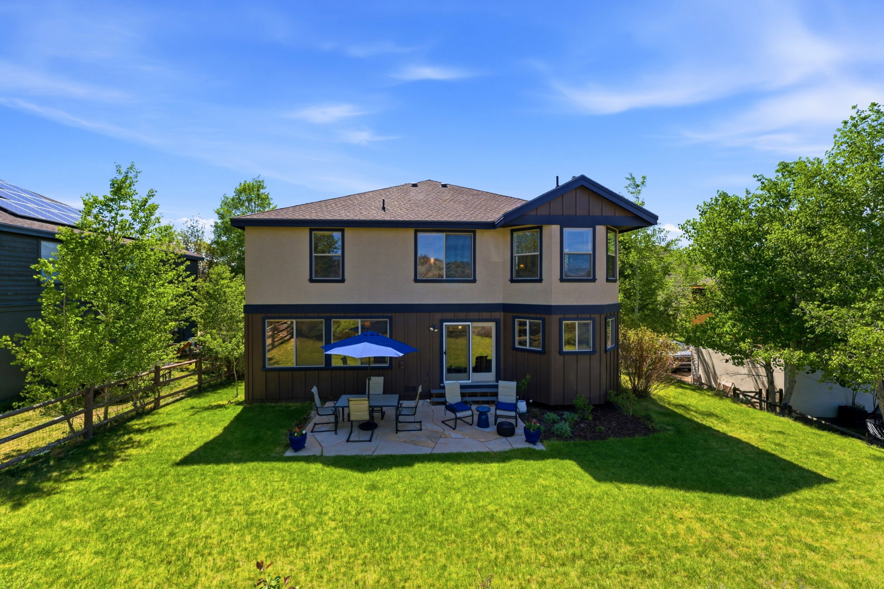Rear exterior featuring a spacious patio, manicured lawn, multiple windows, and a mature tree line