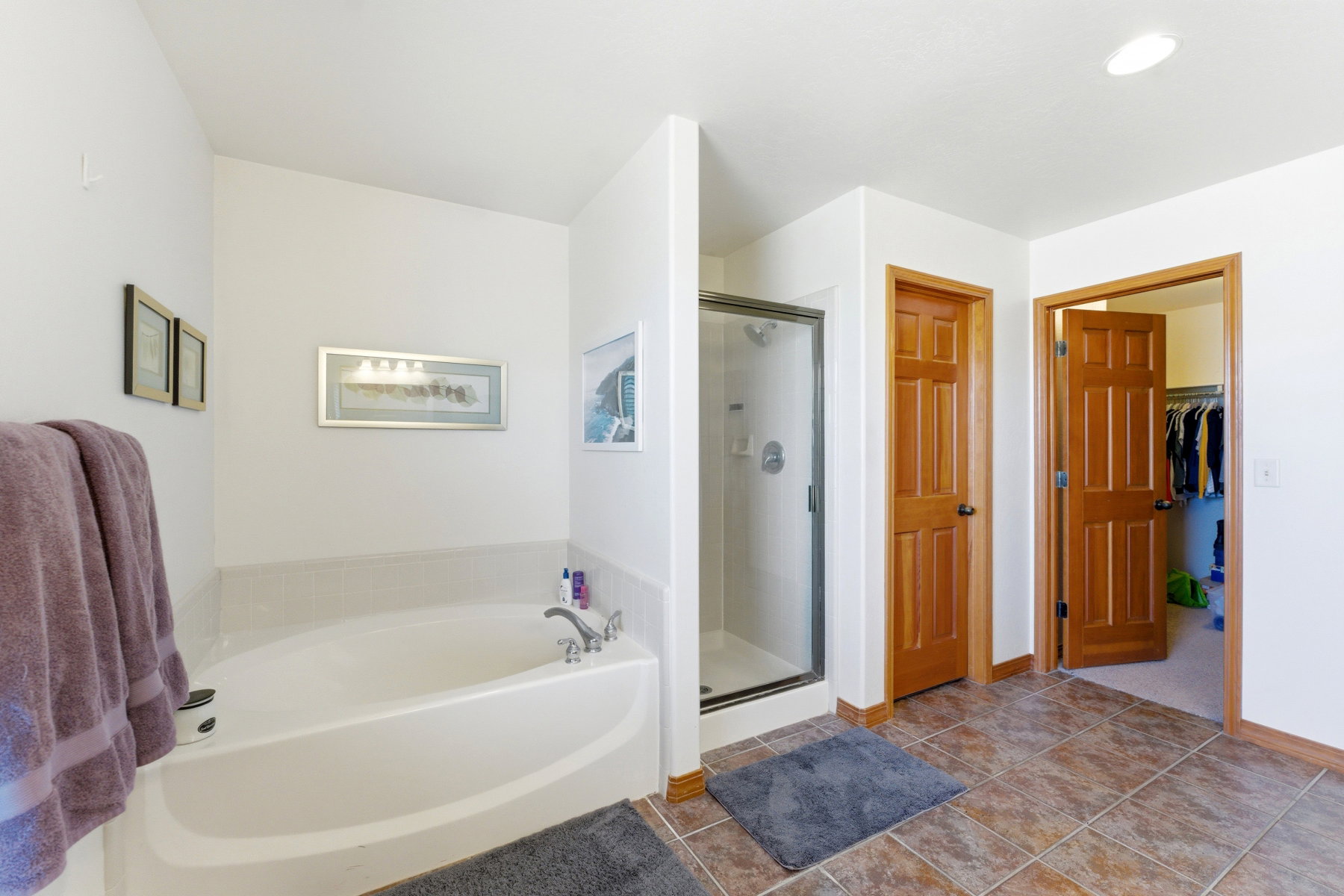 Spacious bathroom featuring an integrated soaking tub, a stand-alone glass-enclosed shower, wood-finish doors, and large format tile flooring