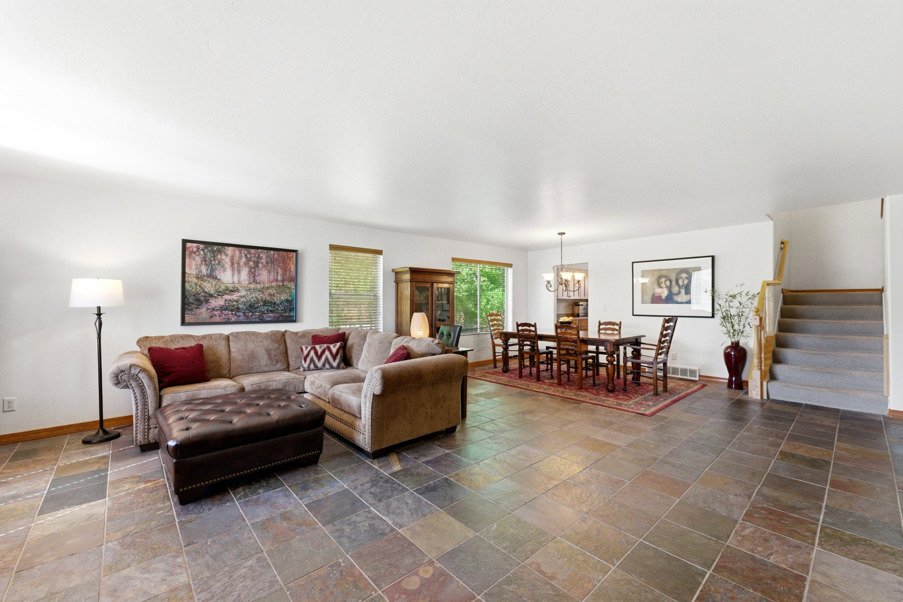 Spacious main level featuring large format multi-tone tile flooring, multiple windows providing natural light, white walls, and a staircase with wood railing and carpeted steps