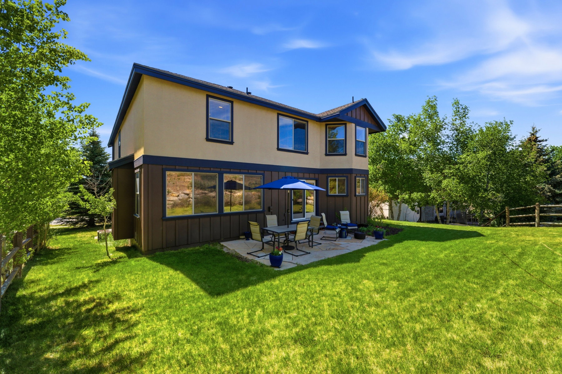 Expansive green lawn surrounds a two-story exterior featuring tan stucco and dark brown siding