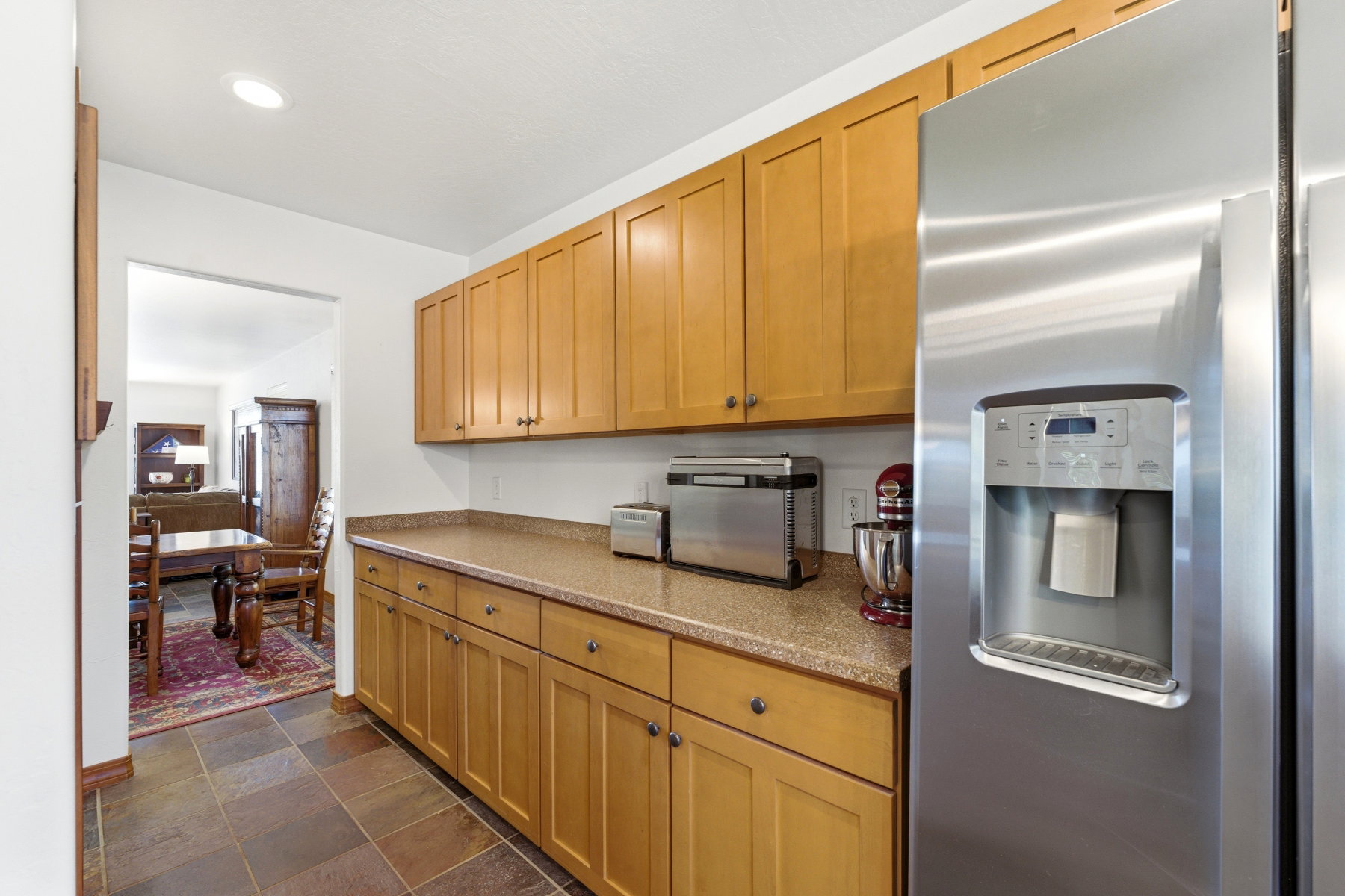 Kitchen featuring extensive light wood cabinetry, a stainless steel side-by-side refrigerator, speckled composite countertops, and large format stone-finish floor tiles