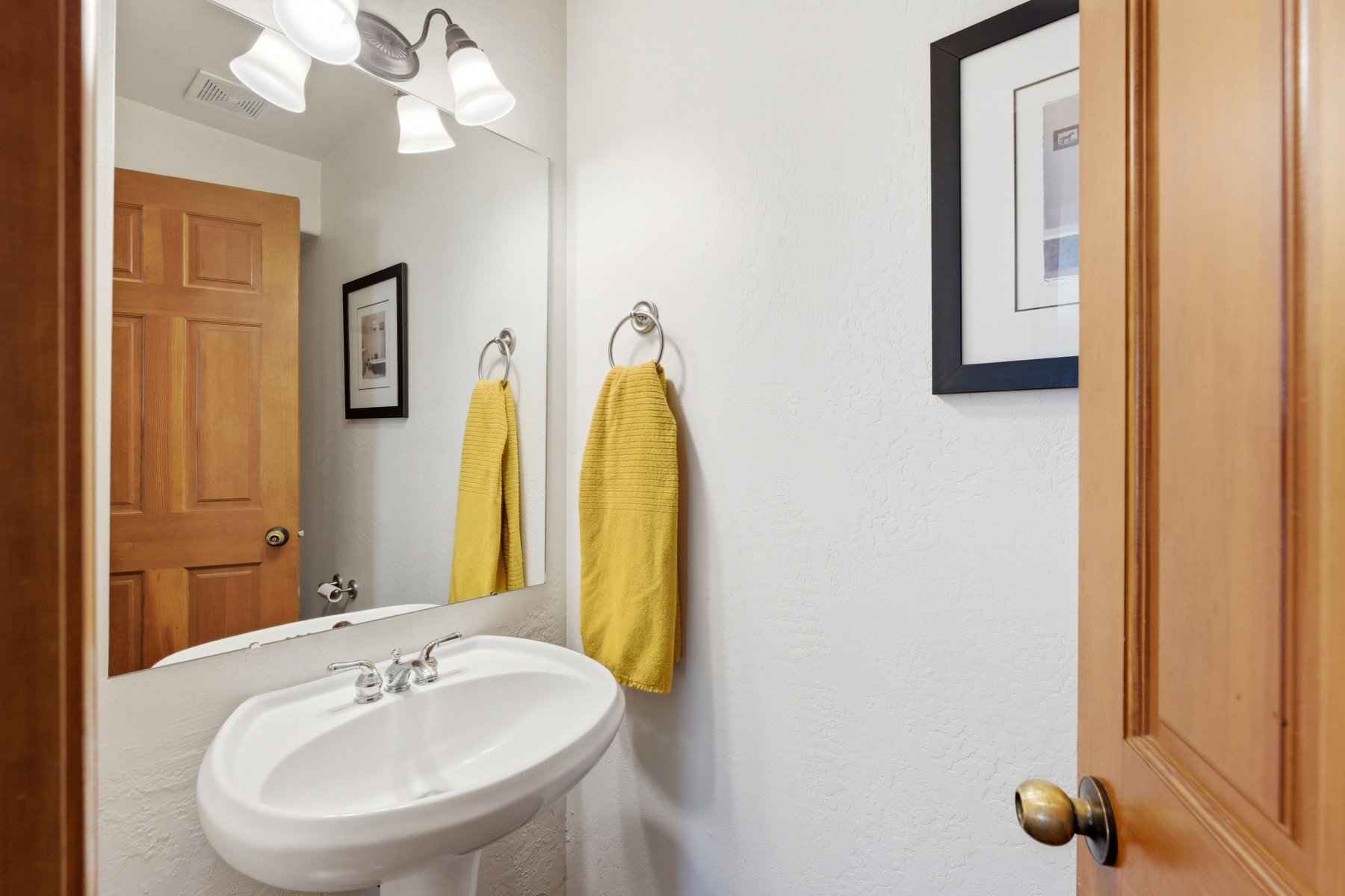 Pedestal sink with chrome faucet, large wall-mounted mirror, and overhead vanity lighting