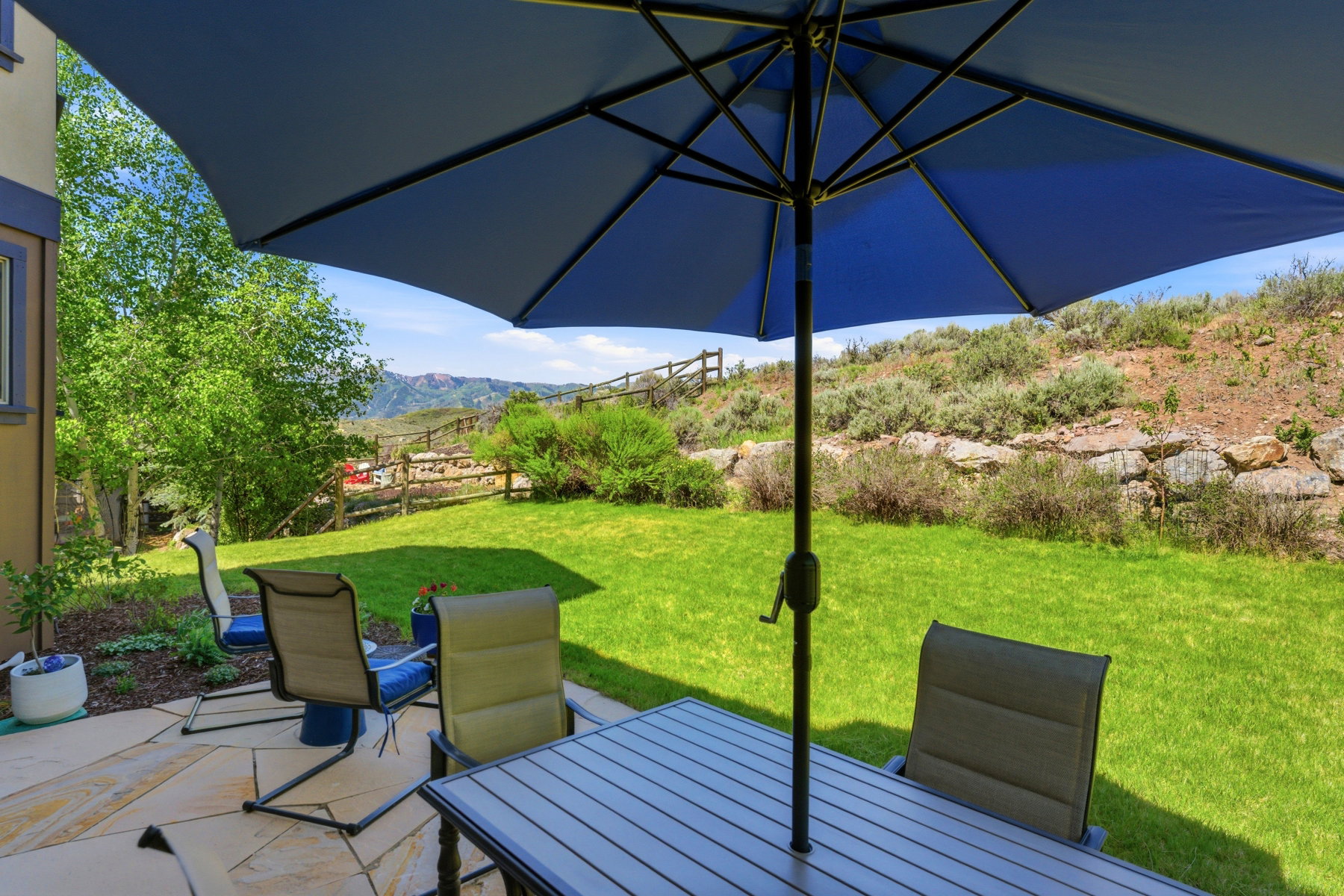 Expansive patio featuring flagstone paving, a lush green lawn, and a natural rock retaining wall