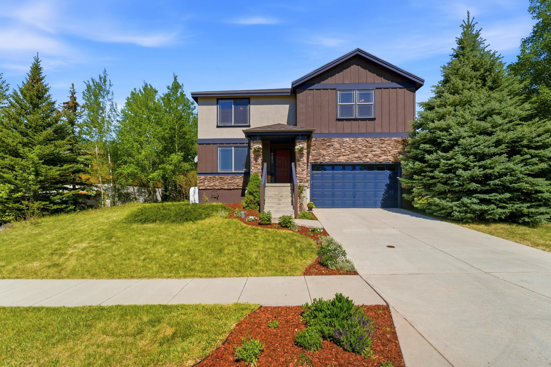 Contemporary multi-level residence featuring a two-car garage with a blue door, stone accents, and brown vertical siding
