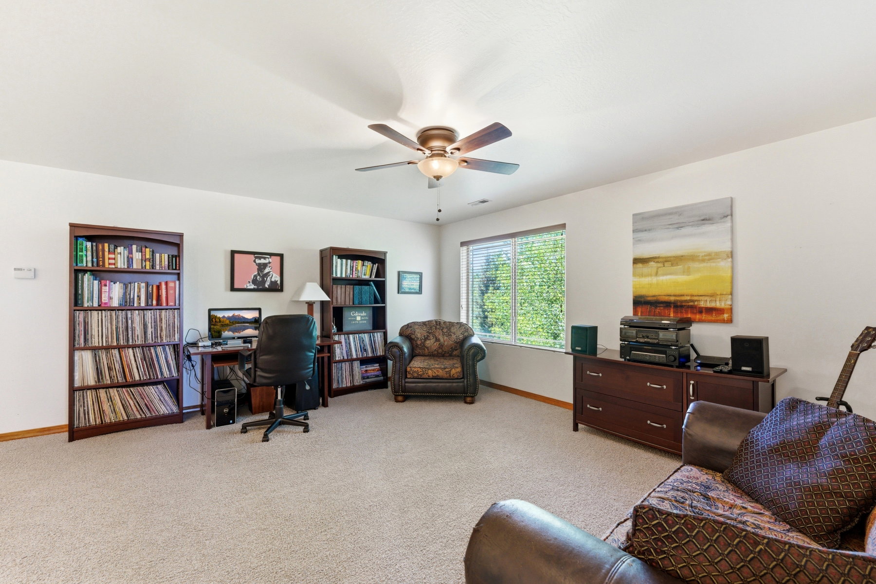 Spacious room featuring carpeted flooring, a ceiling fan with light, and multiple windows providing natural light