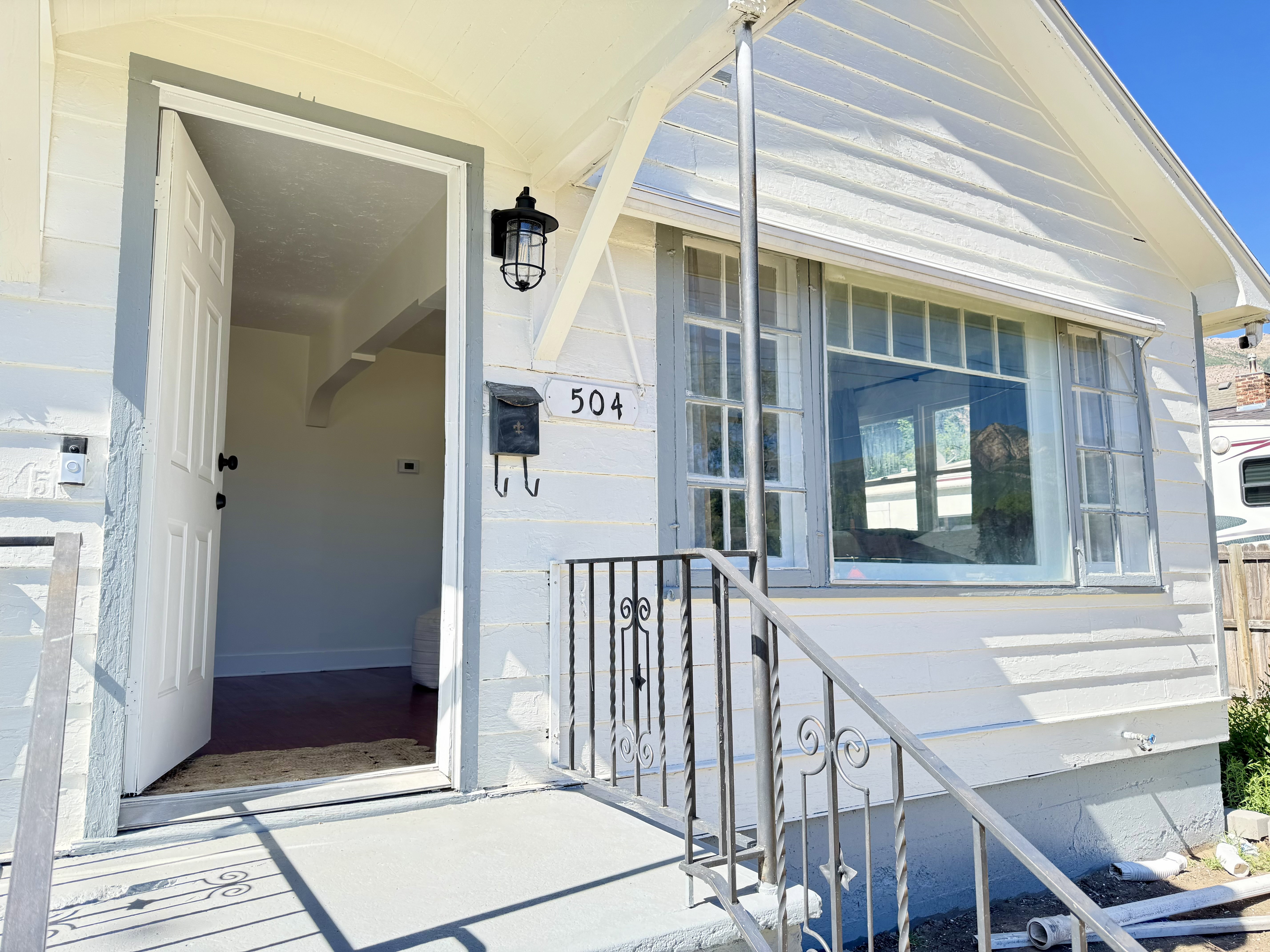 Front exterior showcasing white horizontal siding, a large picture window with transom detailing, and a concrete porch with a wrought iron railing