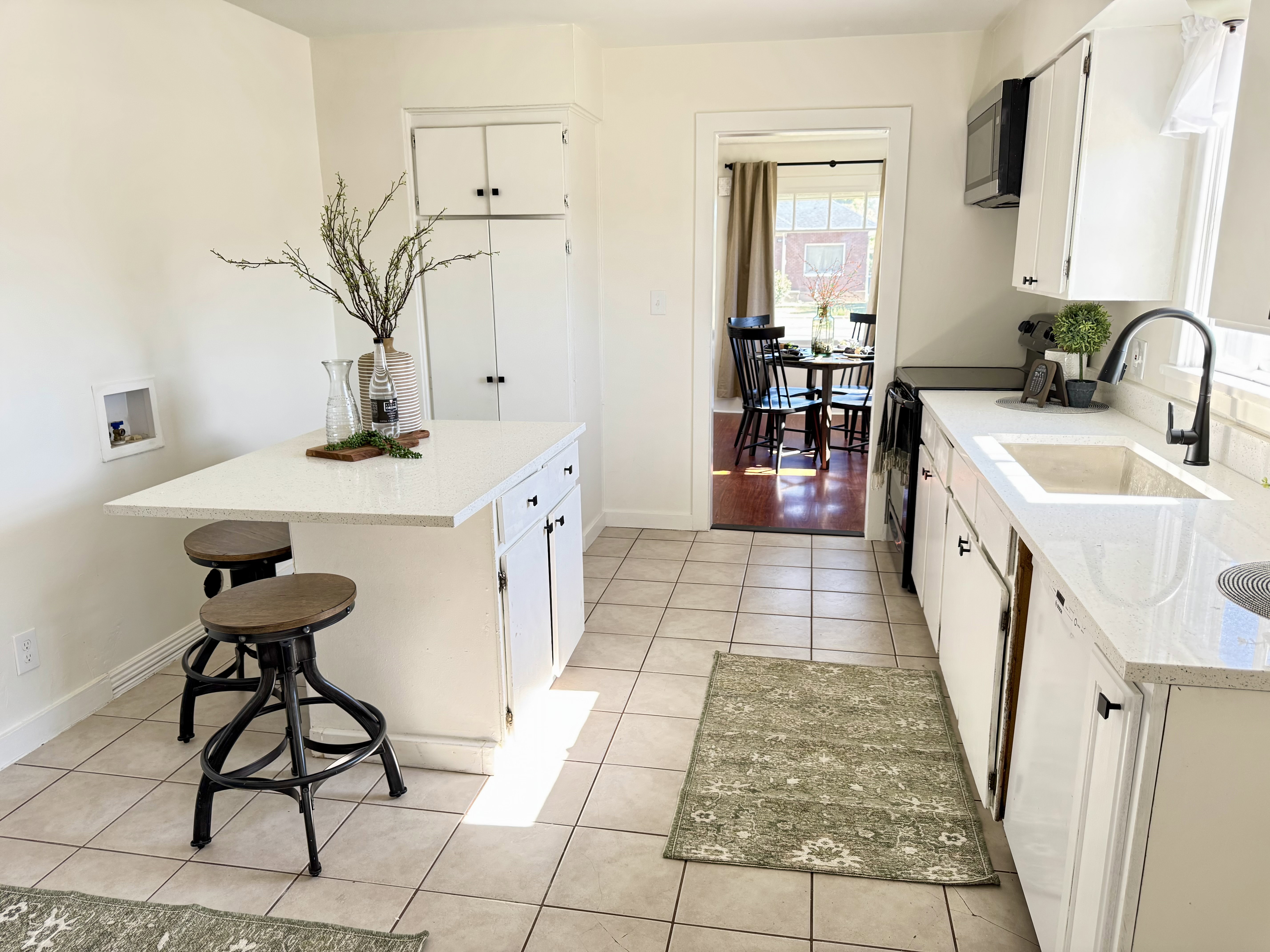 Bright kitchen featuring white cabinetry, light-colored countertops, a built-in kitchen island, a farmhouse-style sink, and a black gooseneck faucet