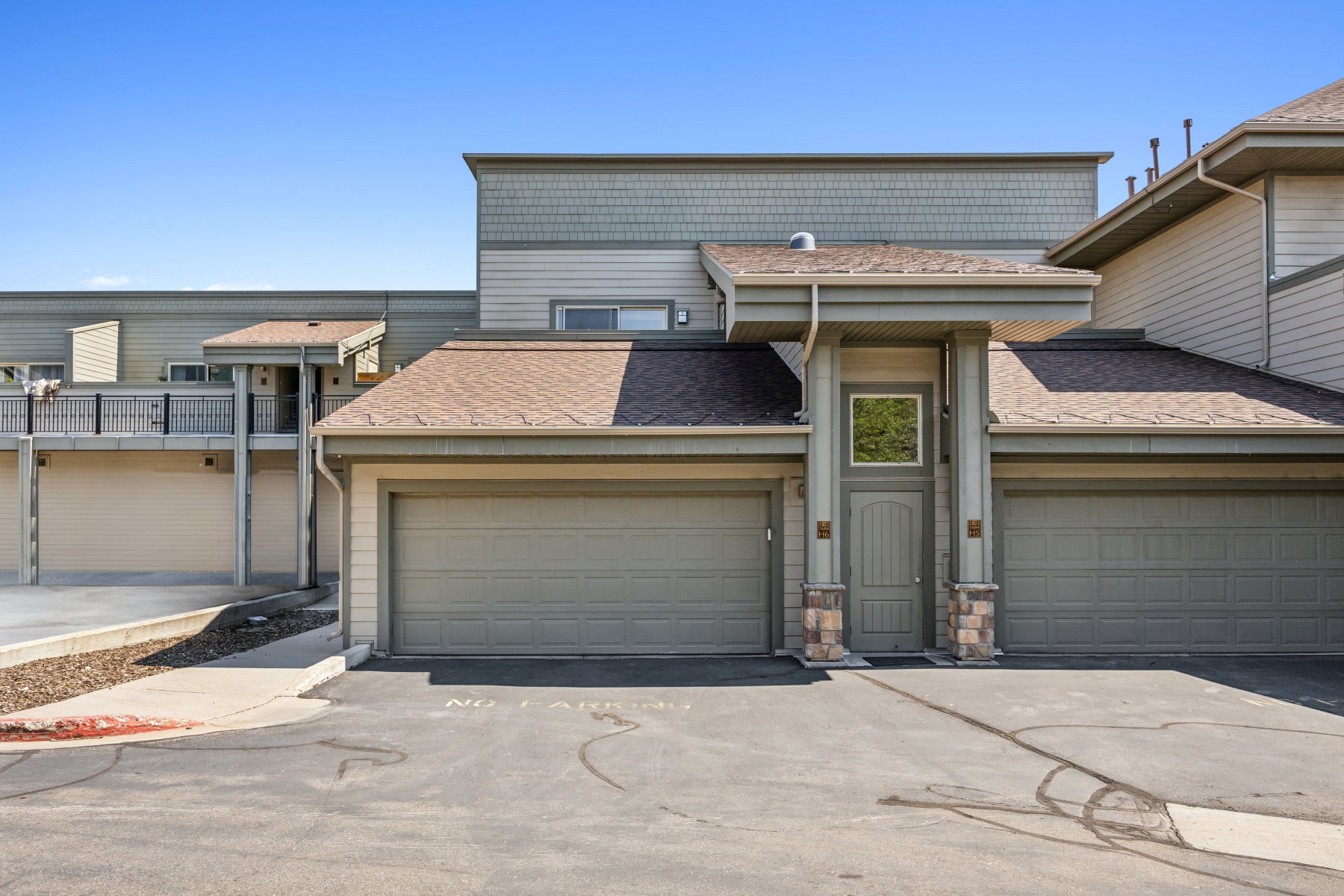Multi-story property featuring horizontal siding, a prominent entry with stone veneer columns, a single entry door with an overhead transom window, and two attached garage bays