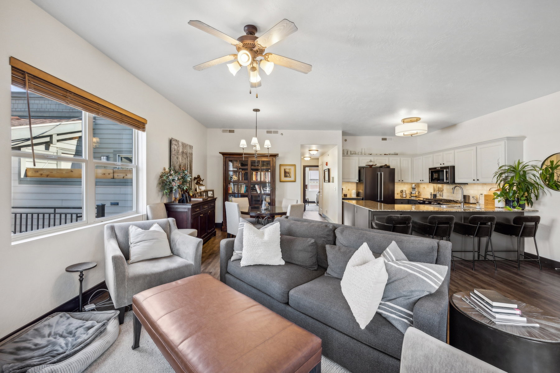 Open-concept living space featuring wood-finish flooring, a contemporary kitchen island with seating, white cabinetry, a built-in ceiling fan, and recessed lighting