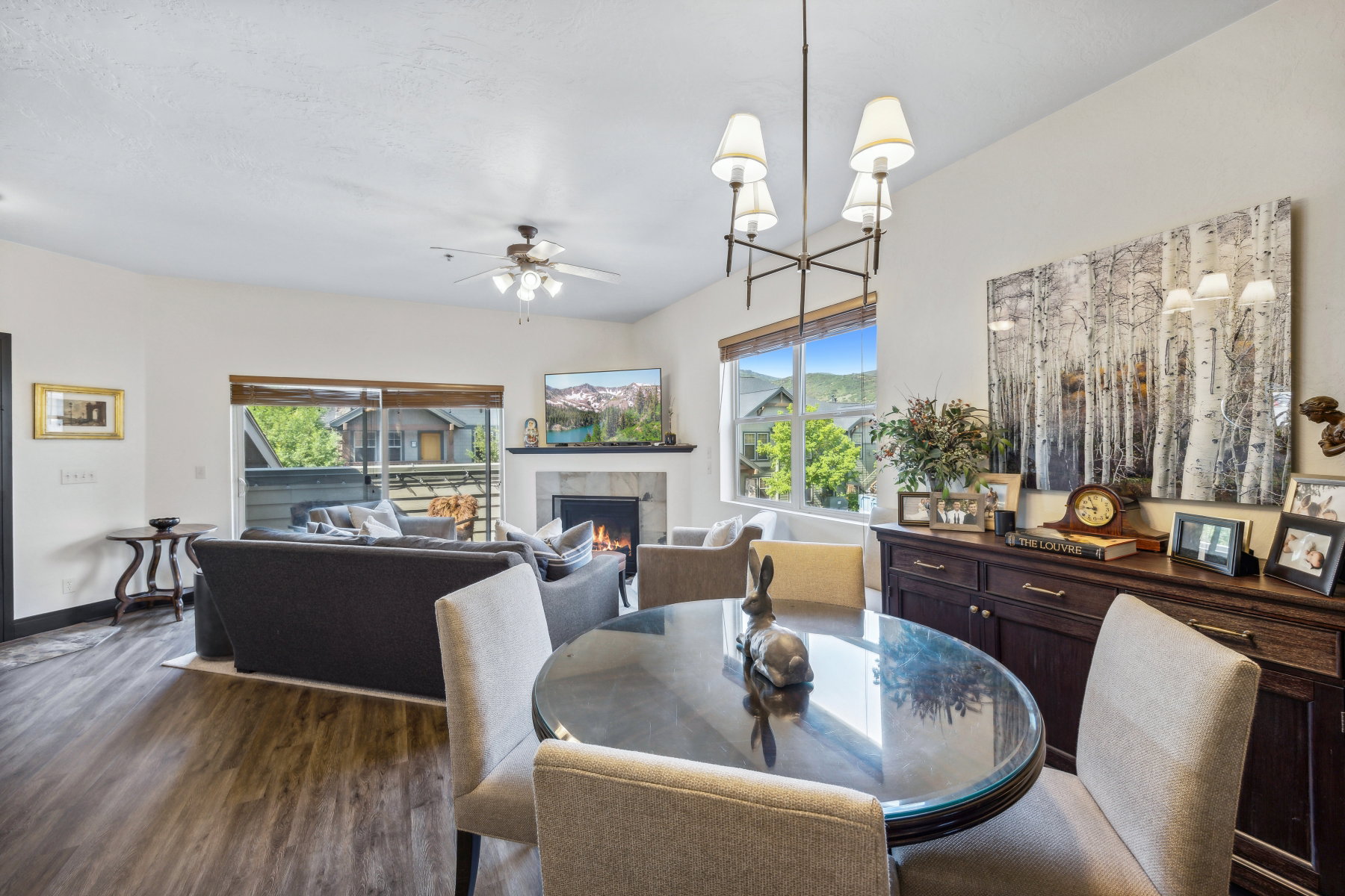 Open-concept living area with wood-finish flooring, a fireplace featuring a stone surround and mantel, and a dining area with a contemporary chandelier