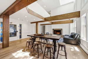 Expansive open-concept living area featuring wood-finish flooring, exposed wood beams, a stone-surround fireplace, and large windows