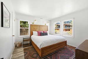 Bright bedroom featuring four windows, wood-finish flooring, and built-in wall sconces