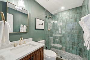 Bathroom featuring a glass-enclosed shower with teal-toned vertical tile and pebble flooring