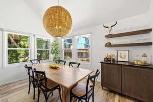 Dining area featuring a vaulted ceiling, wood-finish flooring, and a large woven pendant light fixture