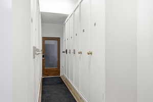 Hallway featuring white paneling, wood-finish flooring, a wooden door with a glass panel, and built-in white cabinetry with various hardware finishes