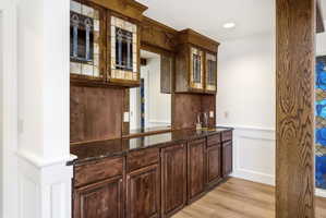 Built-in wet bar featuring dark wood-finish cabinetry, a dark countertop, an undermount sink with a gooseneck faucet, and upper cabinets with decorative glass inserts