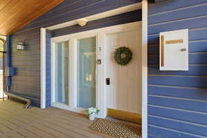 Entryway featuring rich blue siding, a solid white door with black hardware, and two adjacent frosted glass panels