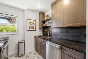 Kitchenette featuring wood-finish cabinetry, stainless steel sink, and a black subway tile backsplash