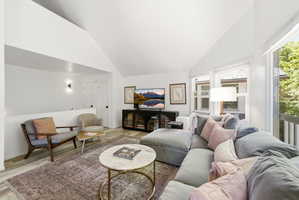 Living area featuring vaulted ceilings, light wood-finish flooring, a wall of windows, white painted walls, and built-in closet doors with dark hardware