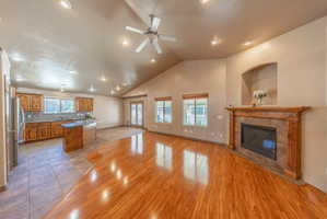 Open-concept living area featuring a vaulted ceiling with recessed lighting and a ceiling fan, wood-finish flooring, and a fireplace with a wood mantel and stone surround
