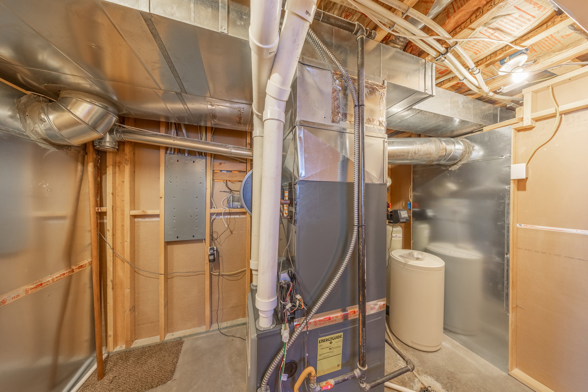 Utility area featuring a furnace, water heater, water softener, exposed ductwork, and electrical conduit