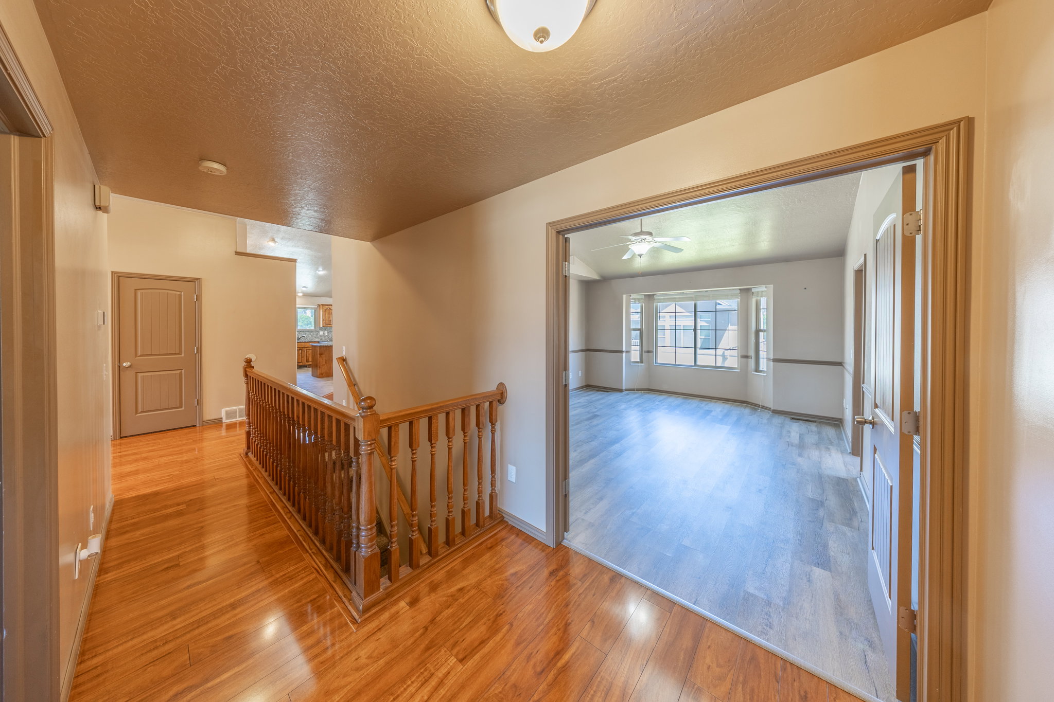 Hardwood-finish flooring throughout the main hallway, featuring a wood spindle railing staircase and a flush mount ceiling light