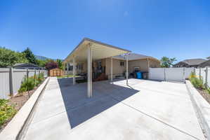 Expansive concrete driveway featuring a full-length carport, a detached storage shed, and a white vinyl privacy fence