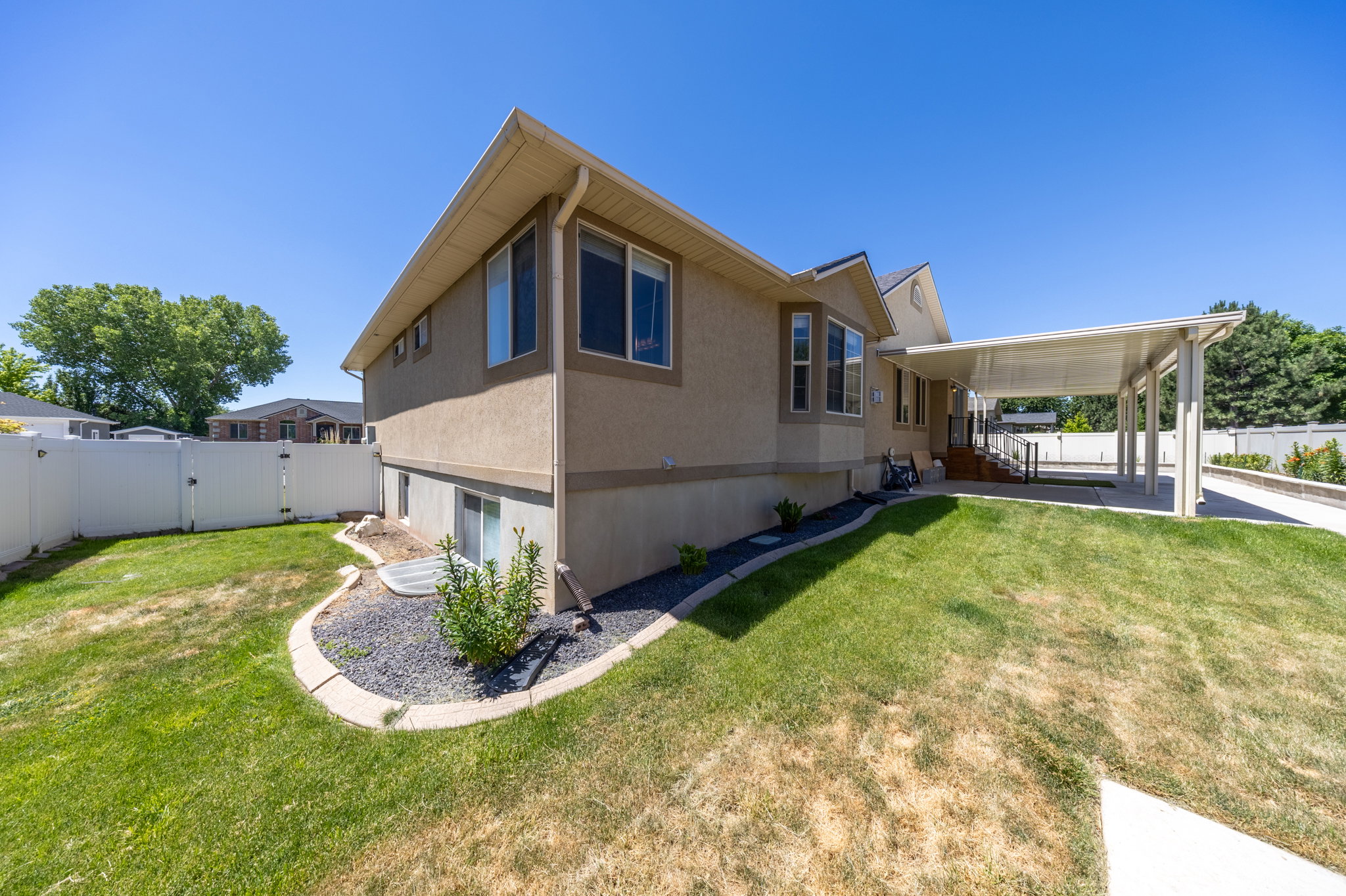 Two-story residence featuring stucco siding, a covered carport, and a white vinyl fence enclosing a portion of the yard