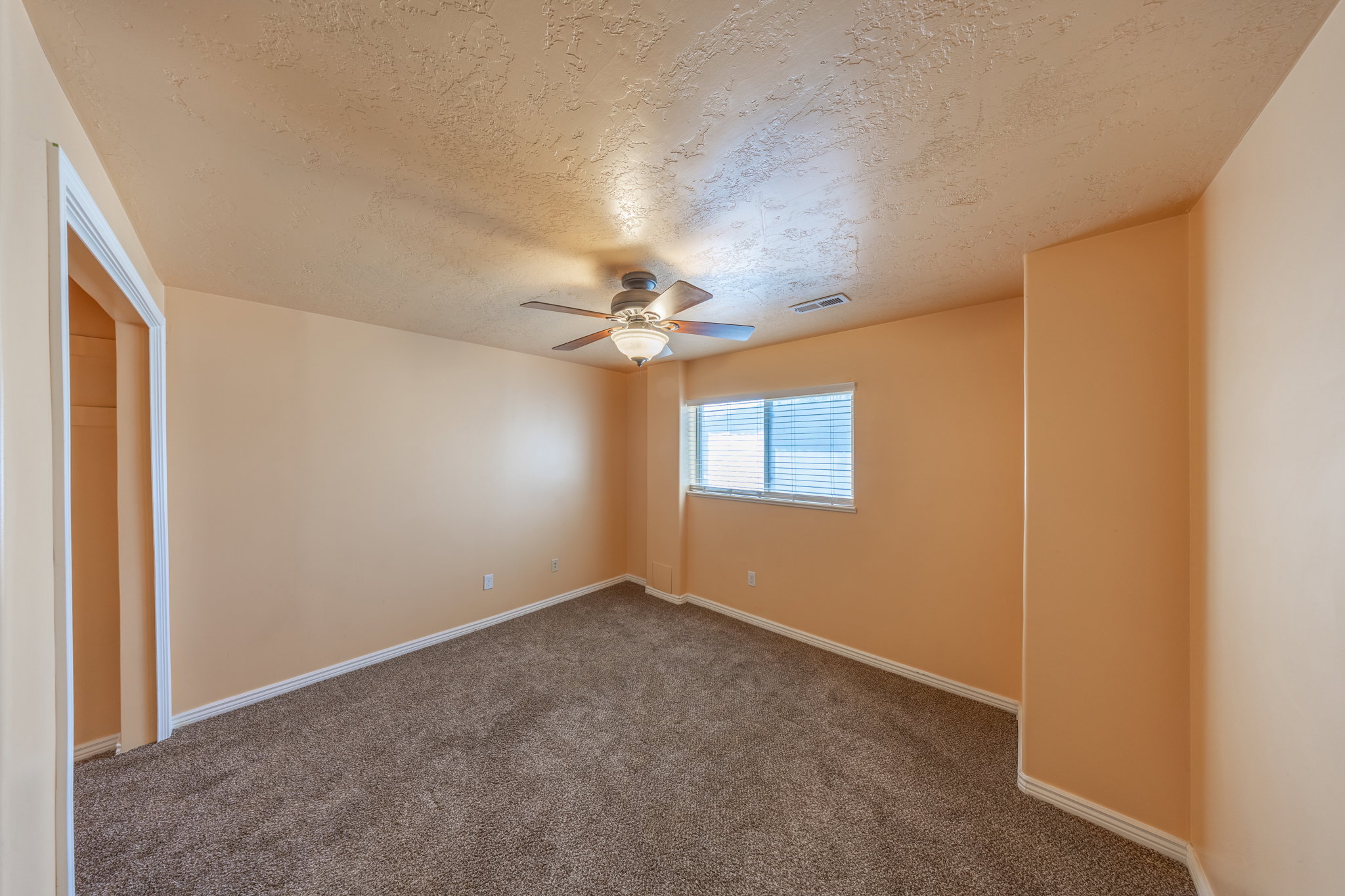 Carpeted room featuring a ceiling fan with integrated lighting, a window with horizontal blinds, and a built-in closet space