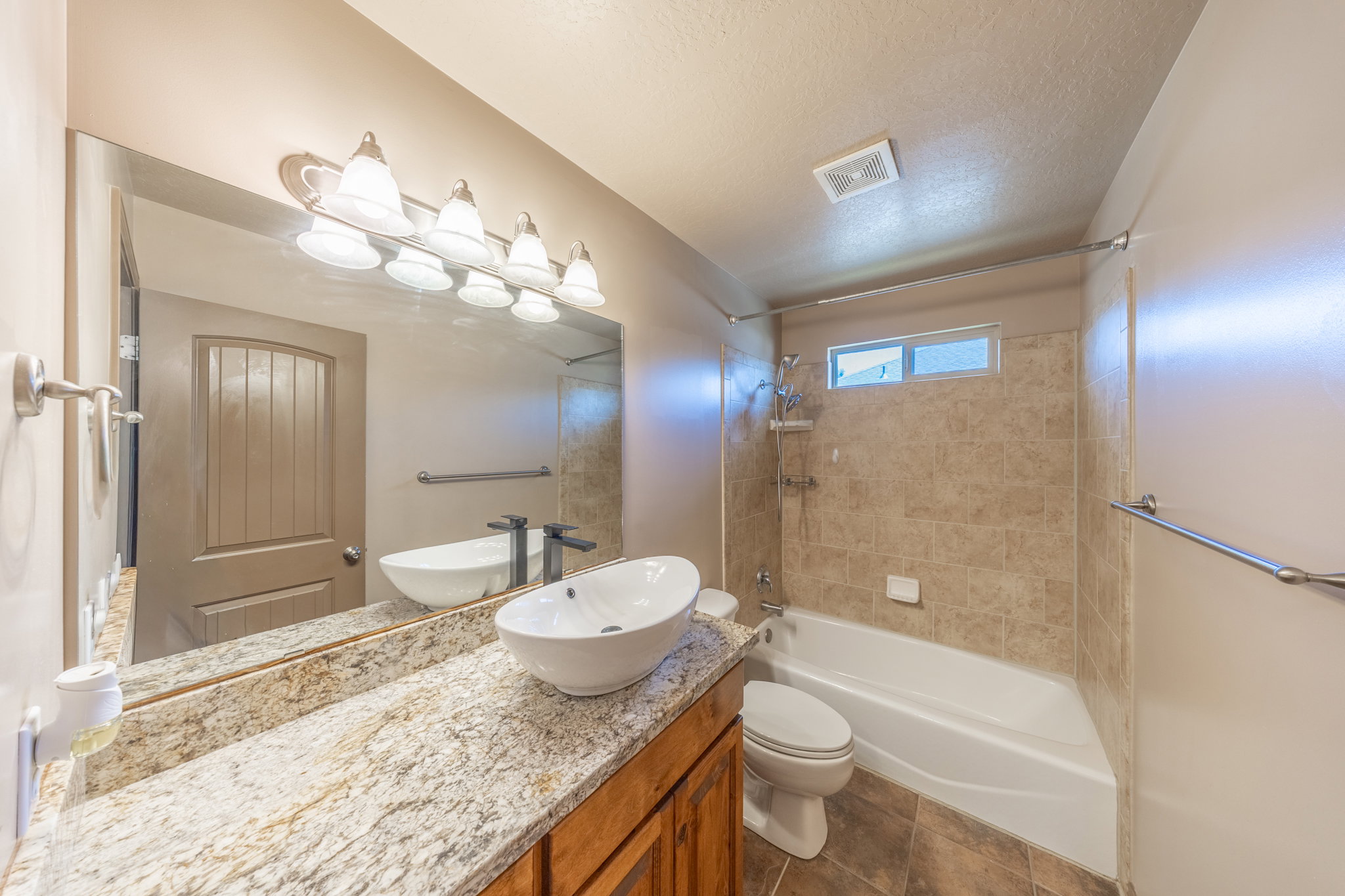 Bathroom featuring a wood-finish vanity with a granite countertop, vessel sink, and an expansive wall mirror