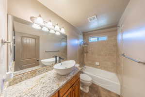 Bathroom featuring a wood-finish vanity with a granite countertop, vessel sink, and an expansive wall mirror