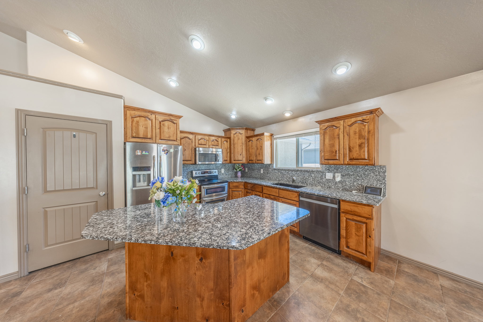 Kitchen featuring a central island with a granite countertop, wood cabinetry, stainless steel appliances, a double-basin sink, and recessed lighting