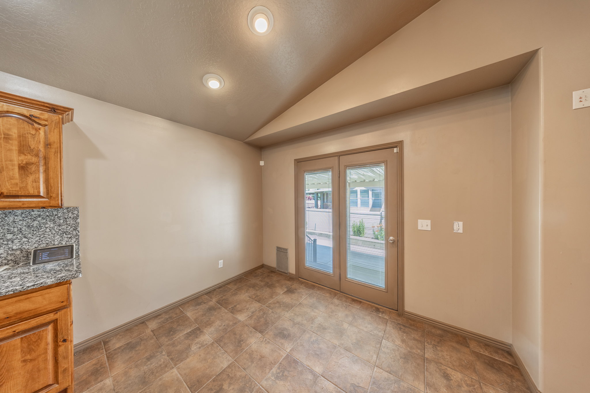 Tiled flooring, double glass panel doors, recessed ceiling lighting, and a partial view of natural wood cabinetry with a speckled countertop