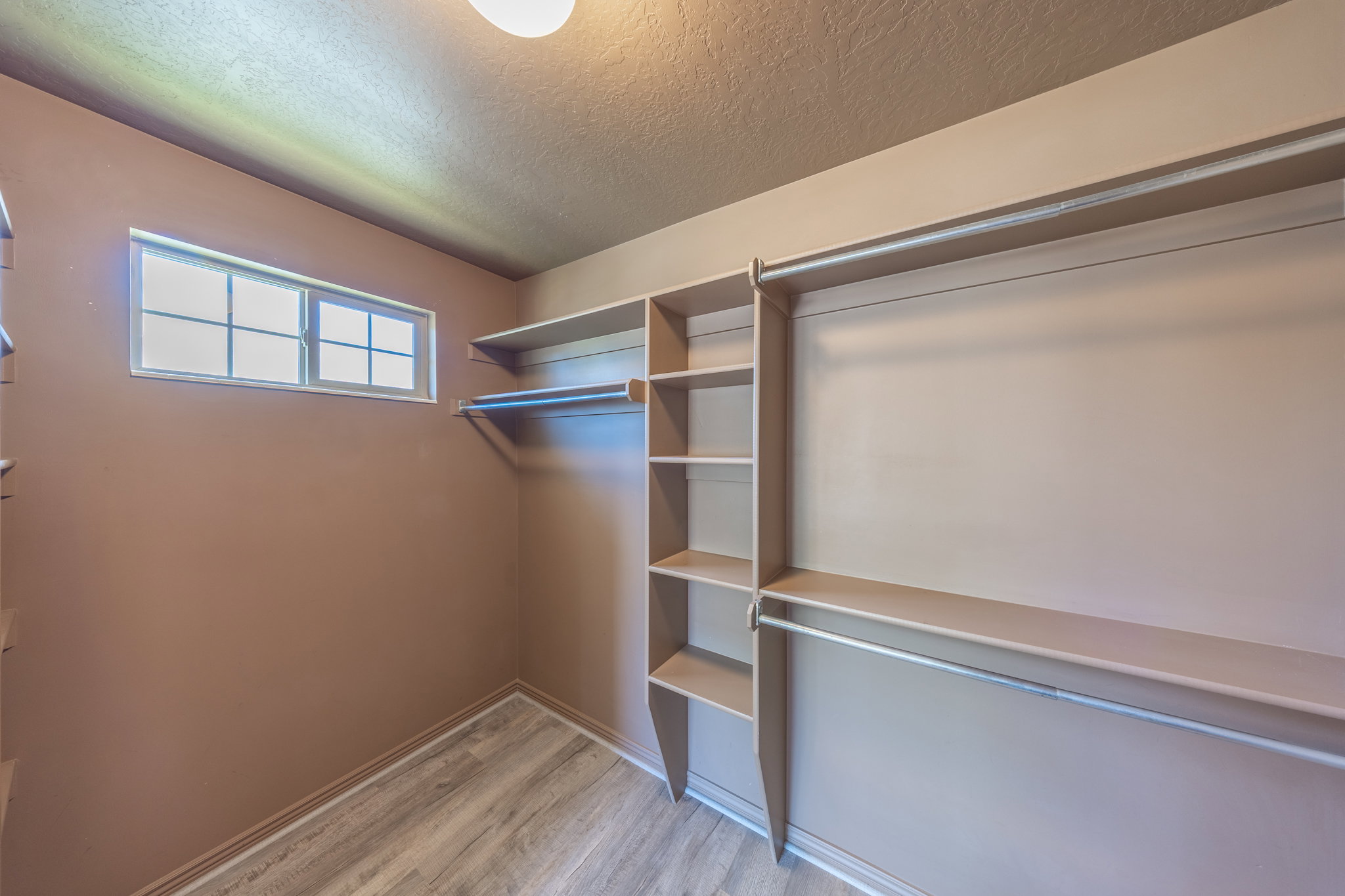Walk-in closet featuring wood-finish flooring, built-in shelving, multiple hanging rods, and a window for natural light