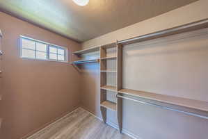 Walk-in closet featuring wood-finish flooring, built-in shelving, multiple hanging rods, and a window for natural light