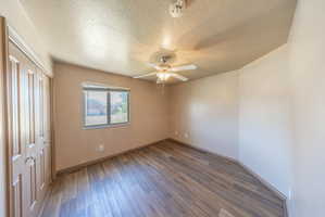 Room featuring wood-finish flooring, a ceiling fan with integrated lighting, and a window with blinds