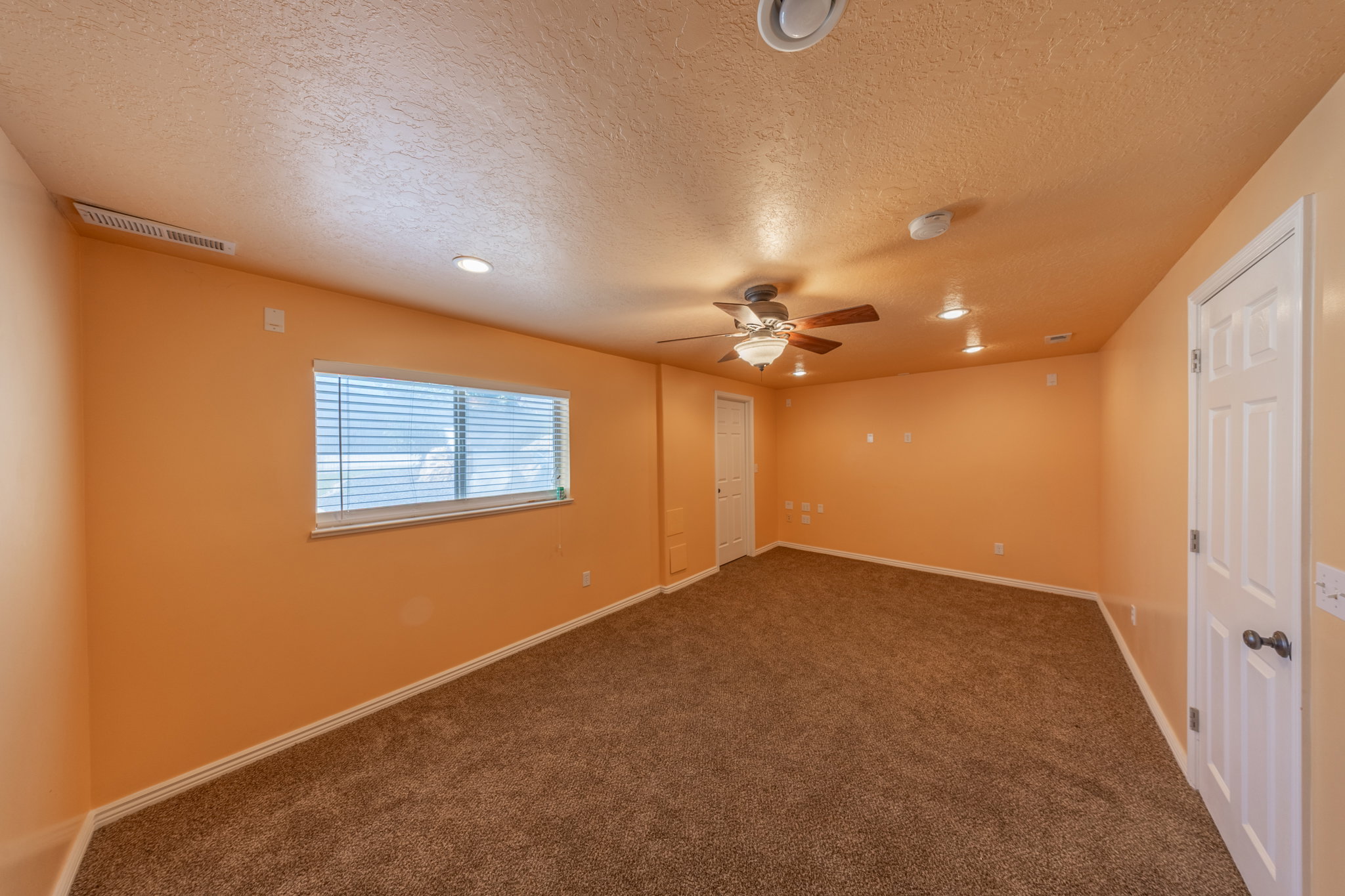 Spacious room featuring brown carpeting, a window with horizontal blinds, recessed lighting, and a ceiling fan with integrated lighting