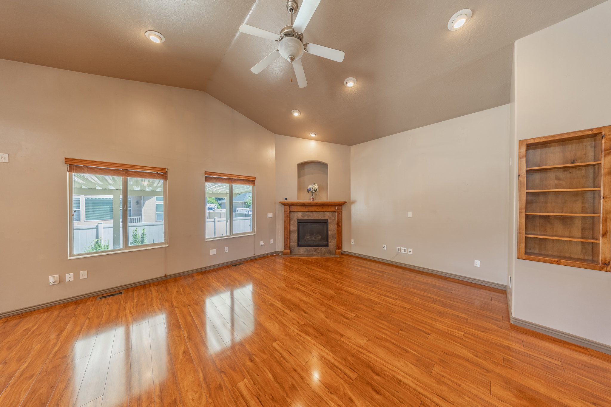 Spacious room featuring vaulted ceilings, recessed lighting, wood-finish flooring, a stone-surround fireplace with a wood mantle, and a built-in wood shelving unit