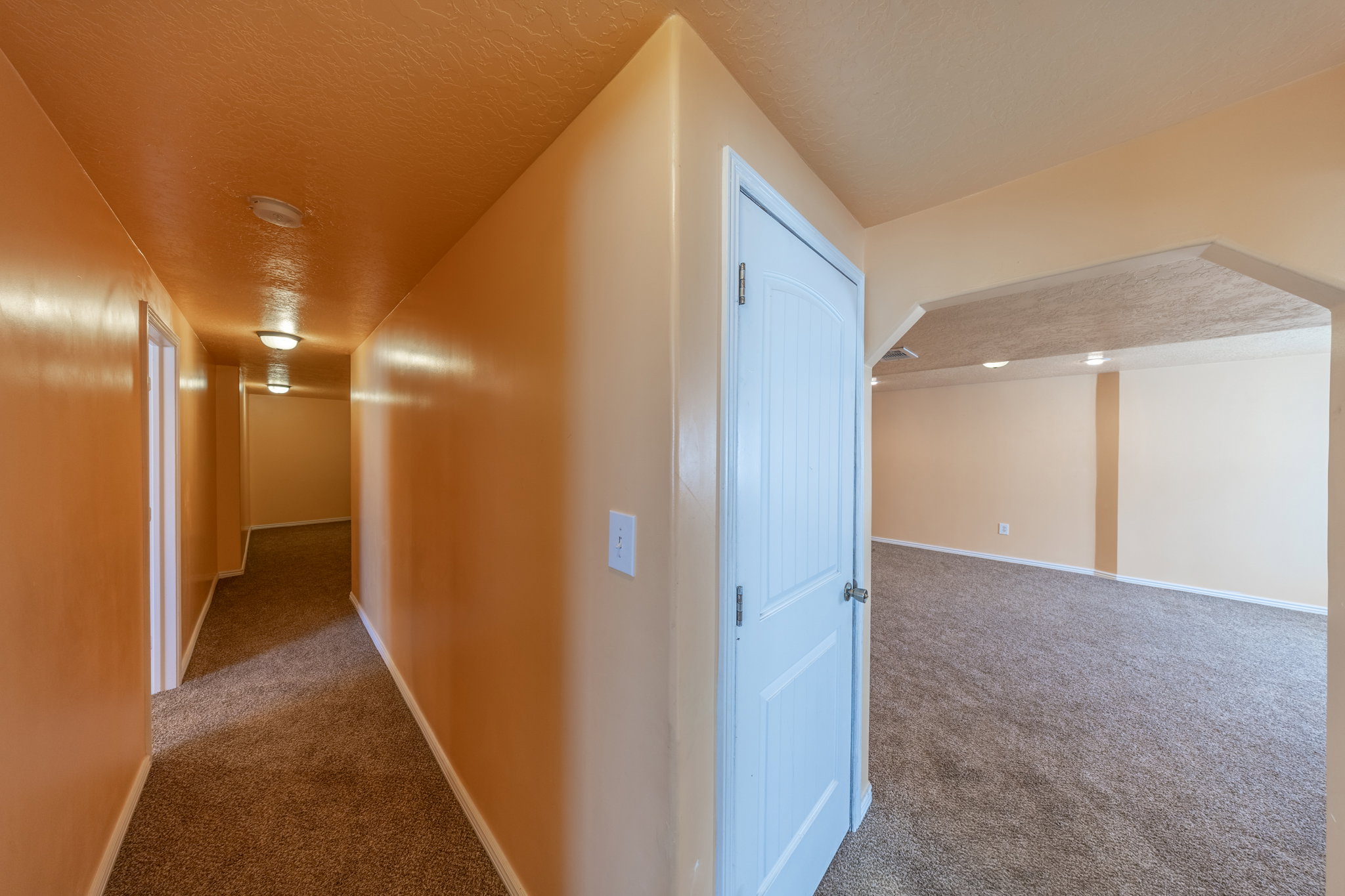 Carpeted hallway with flush-mount lighting, leading to an arched doorway opening to a carpeted room with recessed lighting