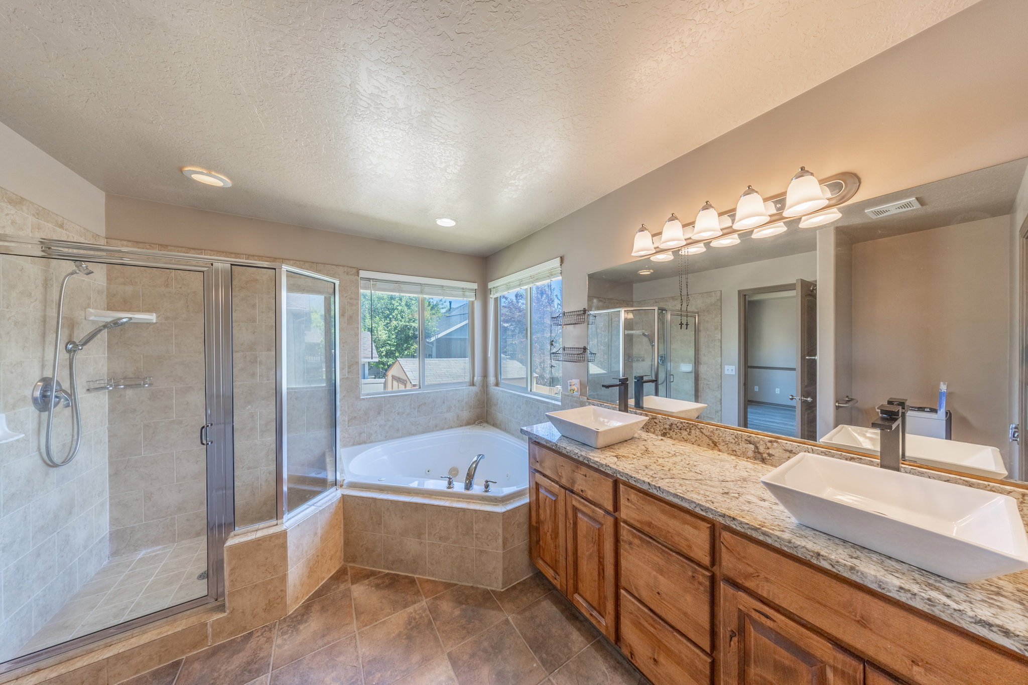 Bathroom featuring a corner soaking tub, glass-enclosed shower with tiled walls, and a double vanity with vessel sinks and a granite-look countertop