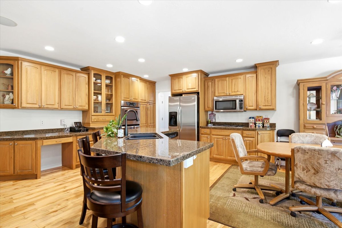 Kitchen featuring wood-finish cabinetry, a large central island with a built-in sink, stainless steel appliances, speckled countertops, and wood-finish flooring