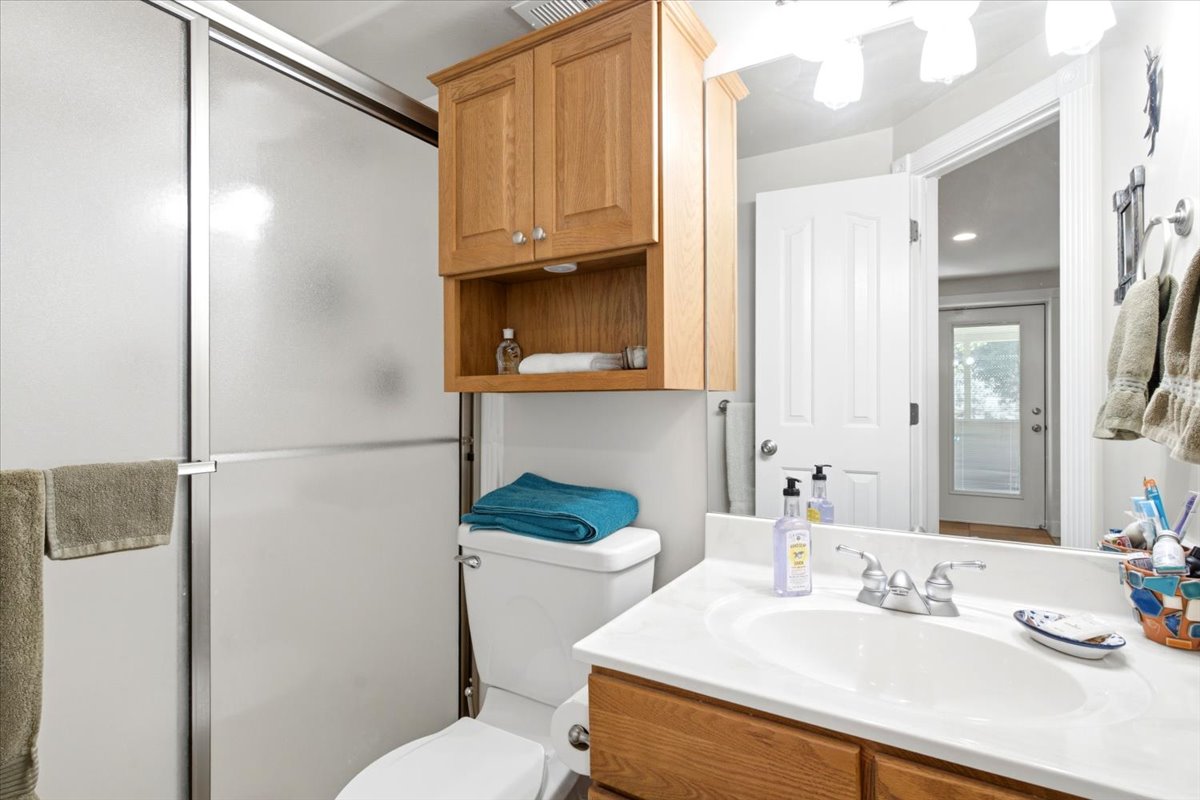 Bathroom featuring a sliding glass shower enclosure, wood-finish cabinetry, white countertop with an integrated sink, and a wall-mounted vanity light fixture